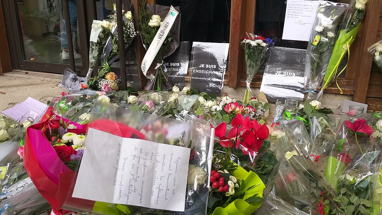 Dépôt de fleurs en hommage à Samuel Paty devant le collège du Bois-d'Aulne, à Conflans-Sainte-Honorine, Par Silanoc — Travail personnel, CC BY-SA 4.0, https://commons.wikimedia.org/w/index.php?curid=95199911